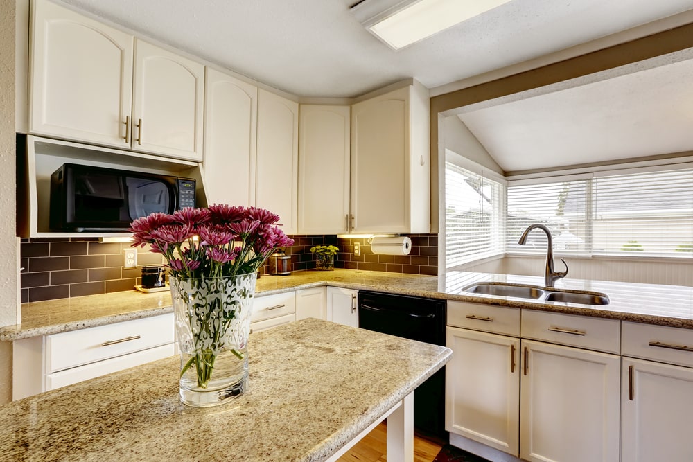 White kitchen cabinets with black appliances. Kitchen island with granite top decorated with flowers